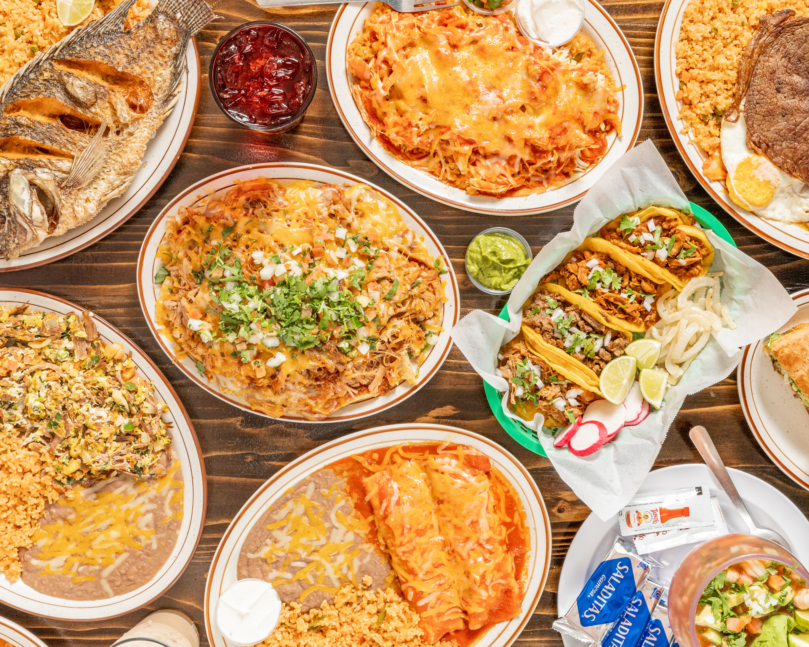 Overhead spread of authentic Mexican catering — tacos, carnitas, fried fish, rice, beans, guacamole and fresh salsa